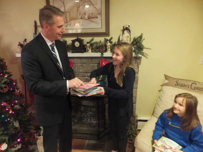 Jim Furgeson, director of community and donor relations for the Newton Medical Center Foundation, accepts some of the books from volunteers Kenzie Merwin (L), and Kate Ryan (R)