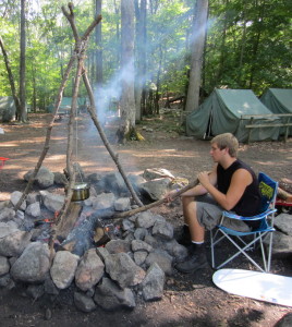 Crew Vice President Chris Rozek cooks part of a meal over a fire using a lashed tripod. Photo courtesy of Venture Crew 276.