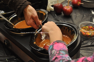 A volunteer helps one of the children dip an apple in caramel and sprinkles. Photo by Jennifer Jean Miller.